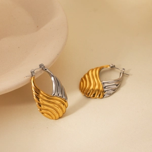 Close-up of gold and silver two-tone hoop earrings with wave texture on beige surface