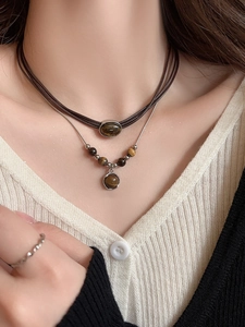 Detail of layered tiger eye pendant necklace with woven cord and silver metal chain