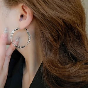 Detail of silver geometric hoop earrings with twisted double line design on model