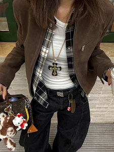 Street style view of long black and gold cross pendant necklace on brown suede jacket