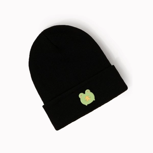Close-up of a black knit beanie with a green cartoon frog patch and fine woven texture