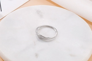 Close-up of a minimalist silver wavy titanium steel ring on white marble surface