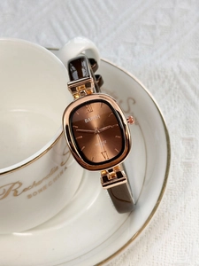 Detail of rose gold tonneau watch with brown dial on vintage porcelain saucer
