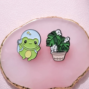 Whimsical enamel pin set featuring astronaut frog and wood spirit plant on a tray