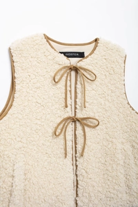 Close-up of cream fleece vest with brown contrast binding and bow tie closures