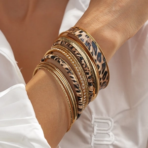 Dettaglio di 10 bracciali dorati impilabili con stampa leopardata e motivi incisi