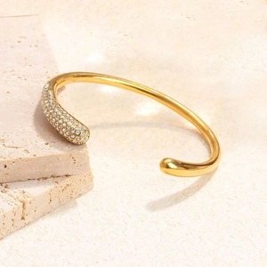 Bracelet jonc doré ouvert orné de strass blancs pavés sur un fond en pierre