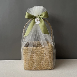 Detail of seagrass gift basket with white mesh wrap, green ribbon and thank you tag