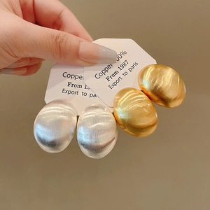 Primo piano di orecchini ovali minimalisti in metallo spazzolato, finiture oro e argento.