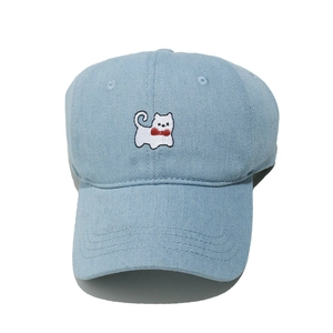 Close-up of light blue denim baseball cap featuring detailed small white cat embroidery