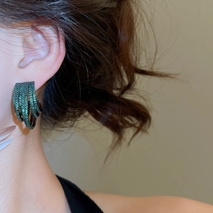 Close-up of multi-layer C-shape green zircon stud earrings on model for luxury look