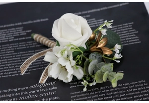 Detail of white artificial rose boutonniere with gold leaves and twine handle on magazine