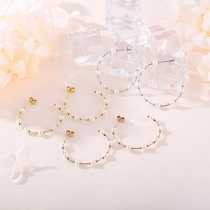 Chic gold C-shaped hoop earrings with white pearls on a minimalist floral backdrop