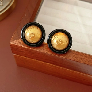 Nahaufnahme von Vintage-Ohrsteckern in Schwarz und Gold mit abstrakten Relief-Details