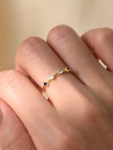 Close-up of a slim gold ring with five gradient blue cubic zirconia stones on a finger