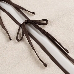 Macro shot of brown satin ribbon bow on cream-colored textured faux shearling jacket fabric