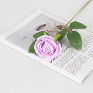 Rosa artificial de terciopelo morado con hojas verdes sobre una revista abierta