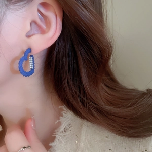 Close-up of blue C-shaped earrings with matte frosted texture and small white bead details