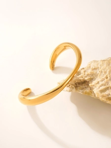 Detailed shot of wave-shaped 18k gold plated stainless steel cuff bracelet on stone