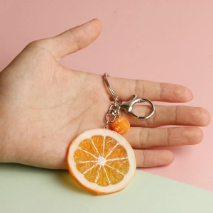 Realistic orange slice keychain with golden citrus texture and metal clasp on colorful background