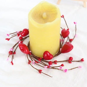 Detail of red heart berry wreath ring surrounding a large pillar candle for romantic decor