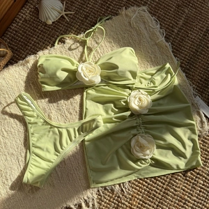Detailed view of green three-piece bikini set with white floral decor on beach mat
