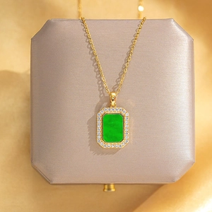 Detail view of a square green gemstone necklace with diamonds on beige velvet box