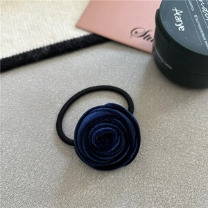 Close-up of a deep blue velvet rose hair tie on a grey textured surface with props