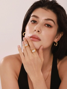 Modella indossa orecchini a cerchio dorati e anelli di conchiglia bianca, set di lusso