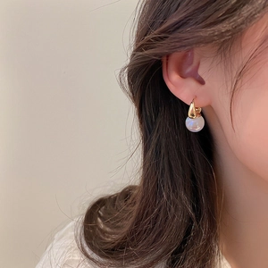 Gros plan d'élégantes créoles dorées avec perle ronde blanche portées par un mannequin