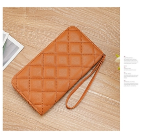 Close-up of orange quilted leather wristlet wallet with gold zipper on wooden surface