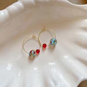Detail of blue bead with orange dots and red bead on golden hoop earring in shell dish