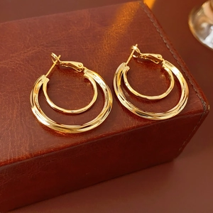 Close-up of luxury gold double hoop earrings placed on a premium dark brown leather gift box