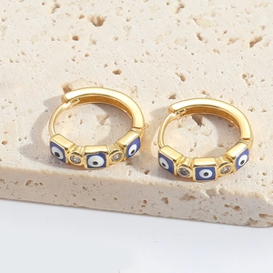 Close-up of gold hoop earrings with blue evil eye zircon on a textured stone base