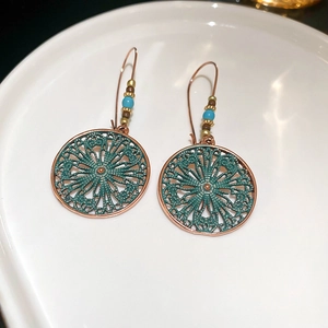 Macro detail of Bohemian hollow flower earrings with vintage turquoise finish in ceramic tray
