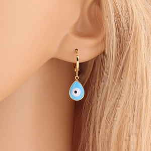 Golden hoop earring with blue evil eye charm shown on a model's ear in close-up view