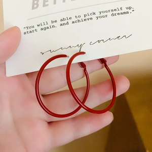 Close-up of vibrant red hoop earrings with polished finish on a white display card