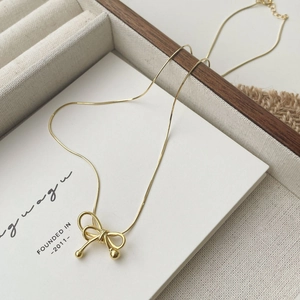 Detail shot of a gold bow pendant necklace with snake chain in a jewelry storage box
