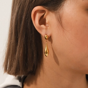 Elegant gold teardrop earrings in polished stainless steel worn by a model in close-up