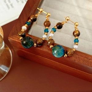 Close-up of vintage hoop earrings with tiger eye beads and teal stones on a wooden box