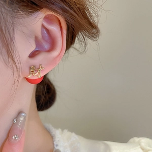 Close-up of golden Chinese character ear studs with red spherical details on model
