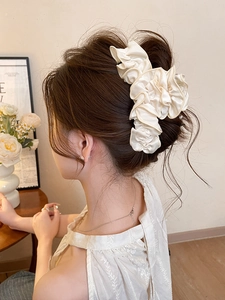 Détail d'une pince à cheveux en satin plissé blanc crème portée sur un chignon bas