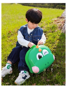 Close-up of a child opening a green dinosaur eggshell backpack on a sunny lawn