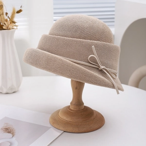 Close-up of beige straw sun hat with delicate ribbon bow on wooden stand