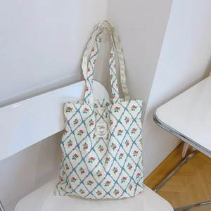 Detail of floral canvas tote bag with blue diamond pattern and red roses on white chair