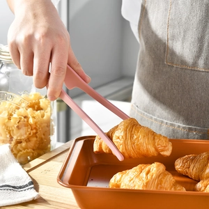 Pink silicone food tongs picking up a croissant in a modern kitchen setting