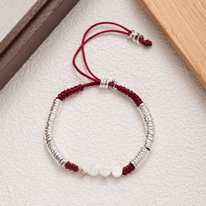 Detailed view of red woven bracelet with silver beads engraved with Ping An Xi Le text