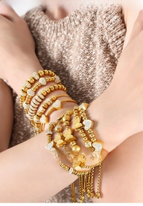 Close-up of stacked gold plated beaded bracelets with heart and butterfly zircon charms