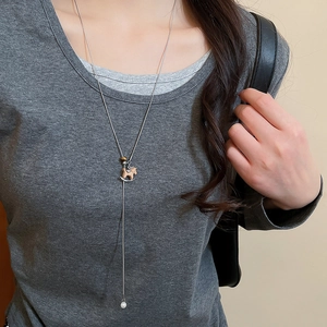 Detail of a silver Y-shaped long necklace with a horse pendant and white pearl on a model