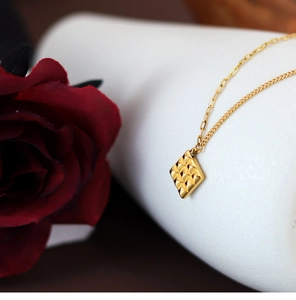 Macro shot of gold-plated square pendant with geometric texture on elegant chain